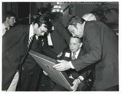 ["Black and white photograph print of Carl Albert and two unidentified men looking at one of Albert's new presents."]