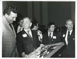 ["Black and white photograph print of Carl Albert and two unidentified men looking at one of Albert's new presents."]