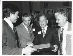 ["Black and white photograph print of Carl Albert and two unidentified men looking at one of Albert's new presents."]