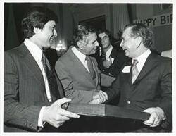 ["Black and white photograph print of Carl Albert and two unidentified men looking at one of Albert's new presents."]