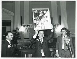 ["Black and white photograph print of Carl Albert holding up his new portrait of Oklahoma football on his birthday. 1976"]