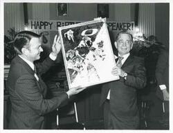 ["Black and white photograph print of Carl Albert holding up his new portrait of Oklahoma football on his birthday. 1976"]