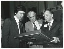 ["Black and white photograph print of Carl Albert holding up his new portrait of Oklahoma football on his birthday. 1976"]