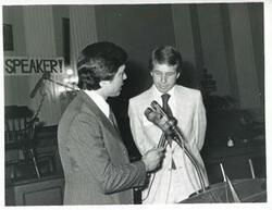 ["Black and white photograph print of two unidentified men speaking into a microphone at Carl Albert's birthday party."]