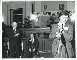 ["Black and white photograph print of an unidentified man speaking at Carl Albert's birthday party. Tom Steed is shown in the background, 1976"]