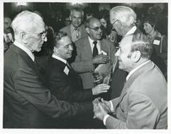 ["Black and white photograph print of Carl Albert shaking hands with an unidentified man. John W. McCormack is also pictured."]