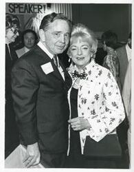 ["Black and white photograph print of Carl Albert standing with Mrs. Dan Flood at his birthday party, 1976"]