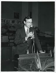 ["Black and white photograph print of an unidentified man speaking at a podium at Carl Albert's birthday party, 1976"]