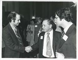 ["Black and white photograph print of Carl Albert at his birthday party shaking hands with an unidentified man. Glen Johnson, Jr. is also shown, 1976"]