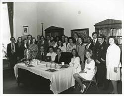 ["Black and white photograph print of Carl Albert, Joel Jankowsky, Loise Butler, Tammy Kitchens, Charles Ward, Sherry Tonubbee, Helen Newman Tuttle, Joe Foote, and others seated and standing in an office. They are preparing to eat cake. May 10, 1974"]
