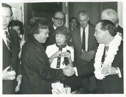 ["Black and white photograph print of Carl Albert shaking hands with an unidentified woman. Mary Albert is in the background. May 10, 1974"]