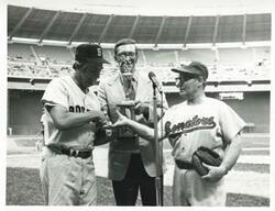 ["Black and white photograph print of three unidentified men standing on the baseball field. 1972"]