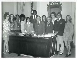 ["Black and white photograph print of Wayne Wells, Loise Butler, Shirley Jeter, Tammy Kitchens, Carl Albert, Sue Thomson, and others standing behind Carl Albert's desk."]
