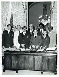 ["Black and white photograph print of John McFall, Hale Boggs, Wayne Wells, Carl Albert, Cynthia Potter, and others posing behind Albert's desk."]