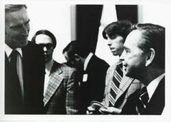 ["Black and white photograph print of Carl Albert speaking with Charlton Heston as others stand nearby."]