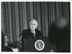 ["Black and white photograph print of Warren Burger speaking at a podium."]