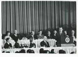 ["Black and white photograph print of Richard M. Nixon speaking at a podium. Warren Burger is seated behind him. National Prayer Breakfast. February 2, 1971"]