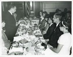 ["Black and white photograph print of Carl Albert speaking to several people seated at a dinner table.+N2827"]