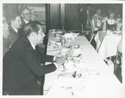 ["Black and white photograph print of Fred Harris seated at a dinner table."]