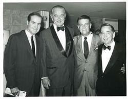 ["Black and white photograph print of Carl Albert, Gerald R. Ford, and two other men seated at a dinner table."]