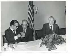 ["Black and white photograph print of Carl Albert, Charles Ward, and David Hall seated at a dinner table."]