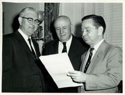 ["Black and white photograph print of Carl Albert, Tom Steed, and Sam Rayburn looking at a document."]