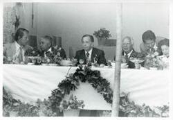 ["Black and white photograph print of Carl Albert and Mary Albert seated at a dinner table with several others during the House delegation trip. August 1975"]
