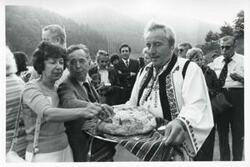["Black and white photograph print of Carl Albert standing with several people at an unidentified function. They are eating some type of food. House delegation trip. August 1975"]