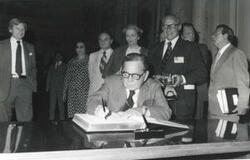 ["Black and white photograph print of Carl Albert signing a guest book as others look on."]