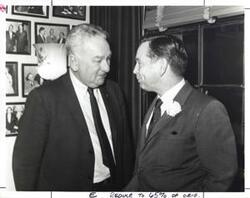 ["Black and white photograph print of Carl Albert speaking with Charles Halleck in an office."]