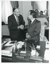 ["Black and white photograph print of Carl Albert shaking hands with an unidentified man."]