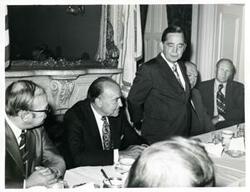 ["Black and white photograph print of Carl Albert speaking to men seated at a dinner table. Gerald R. Ford is present."]