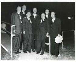 ["Black and white photograph print of Carl Albert posing with Raymond Gary and several other men at a football stadium."]