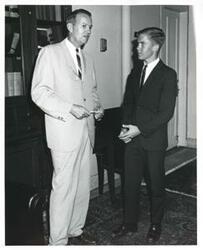 ["Black and white photograph print of two unidentified men speaking to one another"]
