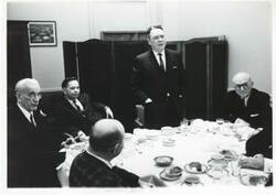 ["Black and white photograph print of Carl Albert, John W. McCormack, Hale Boggs and other men seated at a dinner table."]