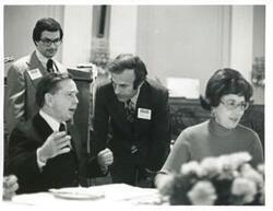 ["Black and white photograph print of Carl Albert speaking with an unidentified man at a reception for freshman members of the 94th Congress. Joel Jankowsky is in the background. December 1, 1975"]