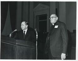 ["Black and white photograph print of Carl Albert speaking at a podium honoring freshman members of the 94th Congress. Another man is standing beside him. December 1, 1975"]
