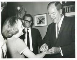 ["Black and white photograph print of Hubert H. Humphrey putting a bracelet on Polly Ritter."]