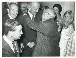 ["Black and white photograph print of Lyndon B. Johnson shaking hands with an unidentified man. Carl Albert and others are pictured."]