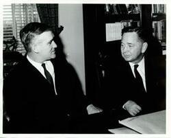 ["Black and white photograph print of Carl Albert seated at his desk with unidentified man."]