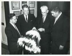["Black and white photograph print of Carl Albert, Hale Boggs, John W. McCormack, and another man standing together. They are looking at an Indian headdress."]