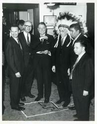 ["Black and white photograph print of Victor Wickersham, Hale Boggs, John W. McCormack (in Indian headdress), Carl Albert, and others."]