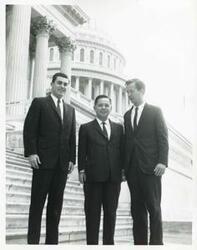 ["Black and white photograph print of Carl Albert posing with Jed Johnson, Jr., and another man on the steps of the Capitol."]