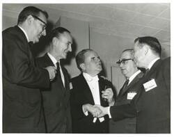 ["Black and white photograph print of Carl Albert shaking hands with an unidentified man. Mike Mansfield and others are also present."]