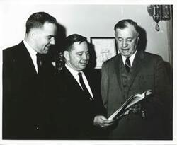 ["Black and white photograph print of Ed Edmondson, Carl Albert, and Michael J. Kirwan looking at a book."]