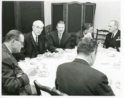 ["Black and white photograph print of Carl Albert, John W. McCormack, Robert S. McNamara, and others seated at a dinner table."]
