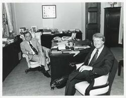 ["Black and white photograph print of Carl Albert seated at his desk. Jimmy Carter is seated also."]