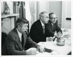 ["Black and white photograph print of Robert Strauss, Russell B. Long, and another man seated at a dinner table at the Democratic leadership conference."]