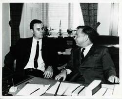 ["Black and white photograph print of Lake Texoma Association President Harold Haddock and Carl Albert discussing the Red River and Lake Texoma development."]