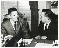 ["Black and white photograph print of Carl Albert seated at his desk. An unidentified man is seated beside him."]